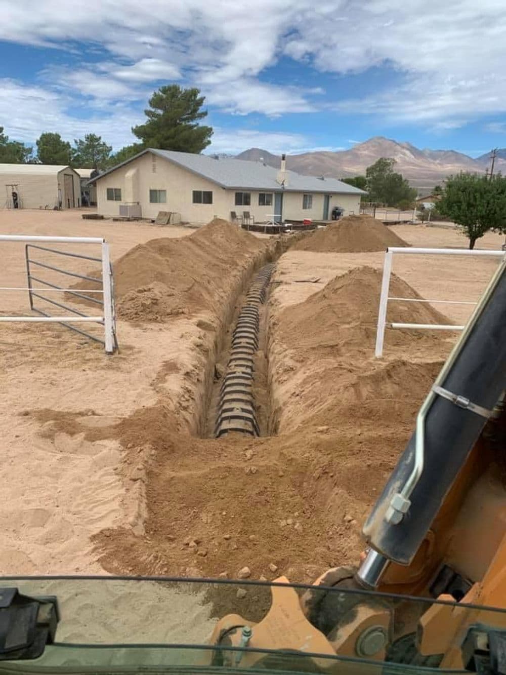 Excavated trench in sandy soil near a house, with machinery visible in the foreground.